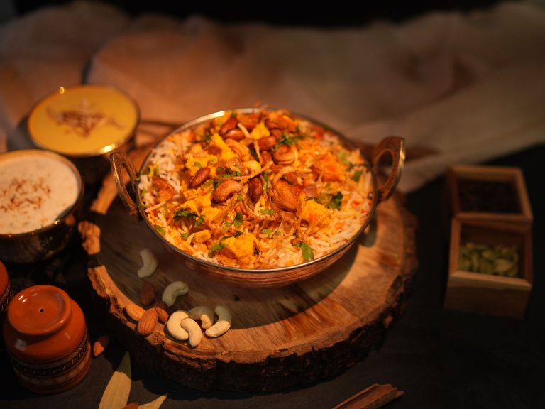 A flavorful bowl of authentic Indian biryani garnished with fried onions and cashews, served with sides.